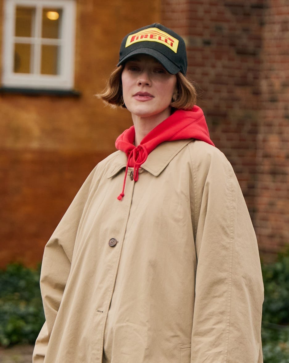 person wearing a beige coat and red hoodie with a pirelli cap