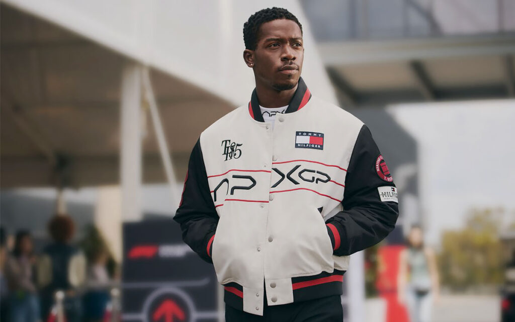 『F1 MOVIE SATIN VARSITY JACKET（税込110,000円）』を着用するジョシュア・ピアース演じるダムソン・イドリス、映画『F1：The Movie（邦題：F1／エフワン）』とトミー ヒルフィガーがコラボした「APXGP」コレクション