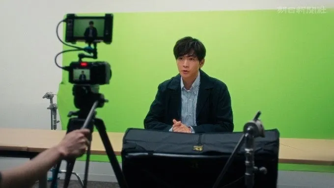 男性がグリーンスクリーンを背景に、カメラの前で話している様子。