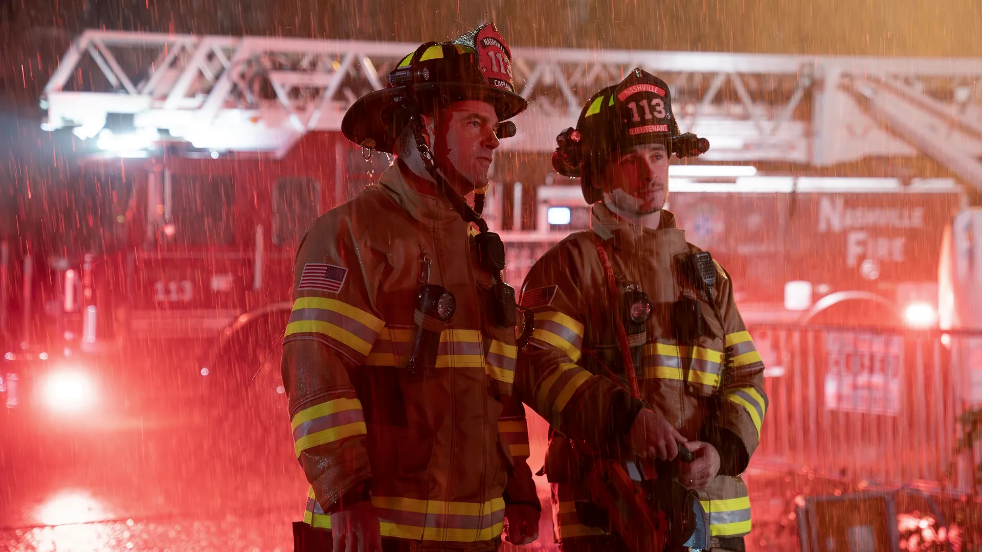 Captain Don Hart (Chris O'Donnell) and Ryan Hart (Michael Provost) stand in the rain in front of a fire truck, lit up red by emergency lights.