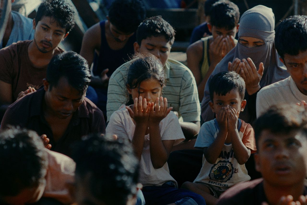 難民船の甲板で大人たちに交じって礼拝する姉ソミーラ（中央）と弟シャフィ　©2025 E.x.N K.K.
